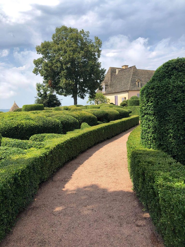 Charming scenic garden with manicured bushes and a winding pathway under a blue sky.